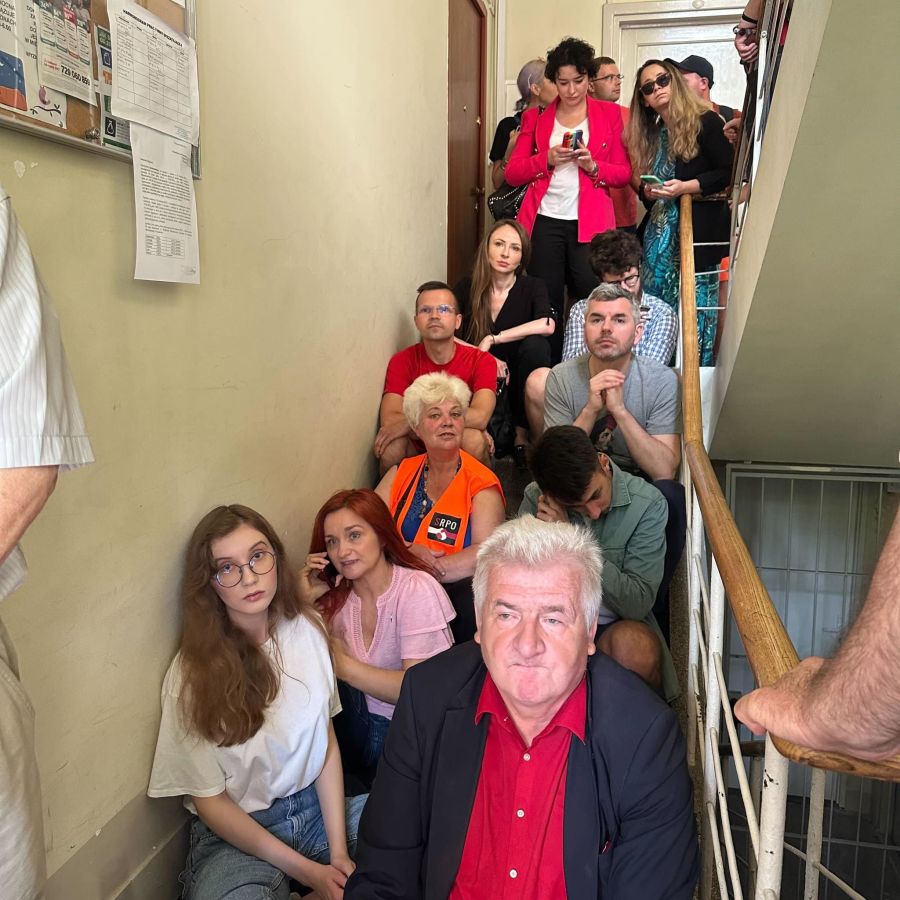 Grupa posłów Lewicy i innych uczestników protestu siedzi na schodach w wąskim korytarzu podczas blokady nielegalnej eksmisji w Warszawie.