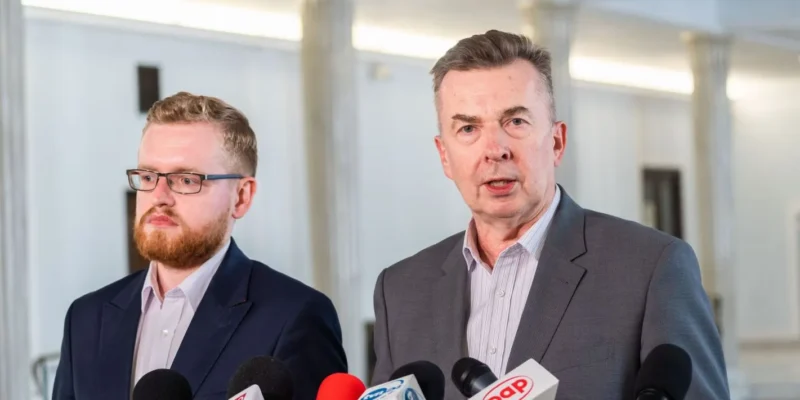 Dwóch mężczyzn w garniturach prowadzi konferencję prasową, przemawiając do mediów zza zestawu mikrofonów, w kontekście fuzji Orlenu z Lotosem i PGNiG.