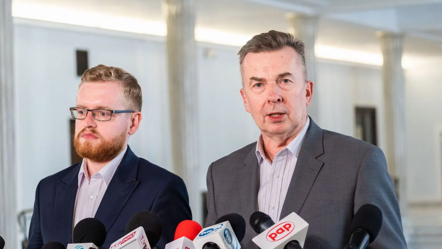 Dwóch mężczyzn w garniturach prowadzi konferencję prasową, przemawiając do mediów zza zestawu mikrofonów, w kontekście fuzji Orlenu z Lotosem i PGNiG.