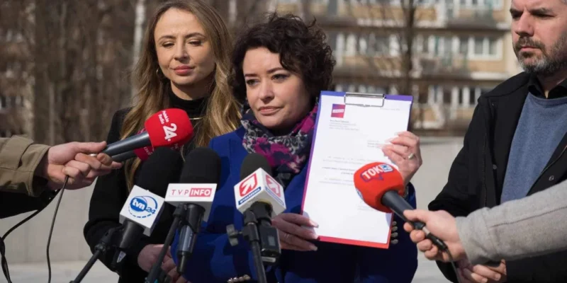 Dwie kobiety stoją na zewnątrz przed mikrofonami mediów i prezentują dokument podczas konferencji prasowej w plenerze.