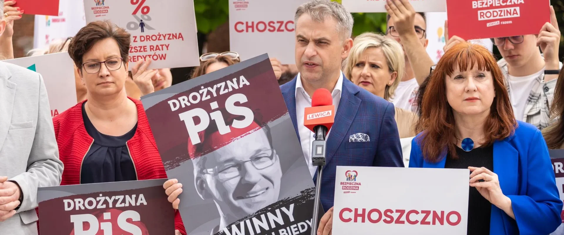 Grupa zwolenników Lewicy podczas wiecu trzyma plakaty anty-PiS i słucha przemówienia wygłaszanego do mikrofonu z logiem Lewicy.