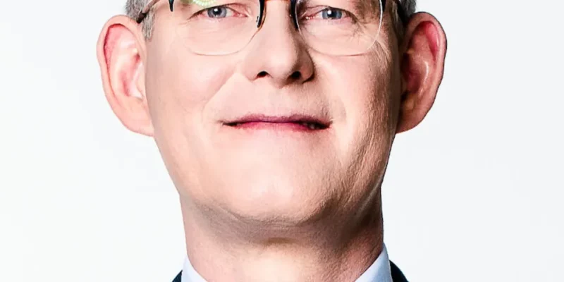 To portret mężczyzny w okularach na jasnym tle.