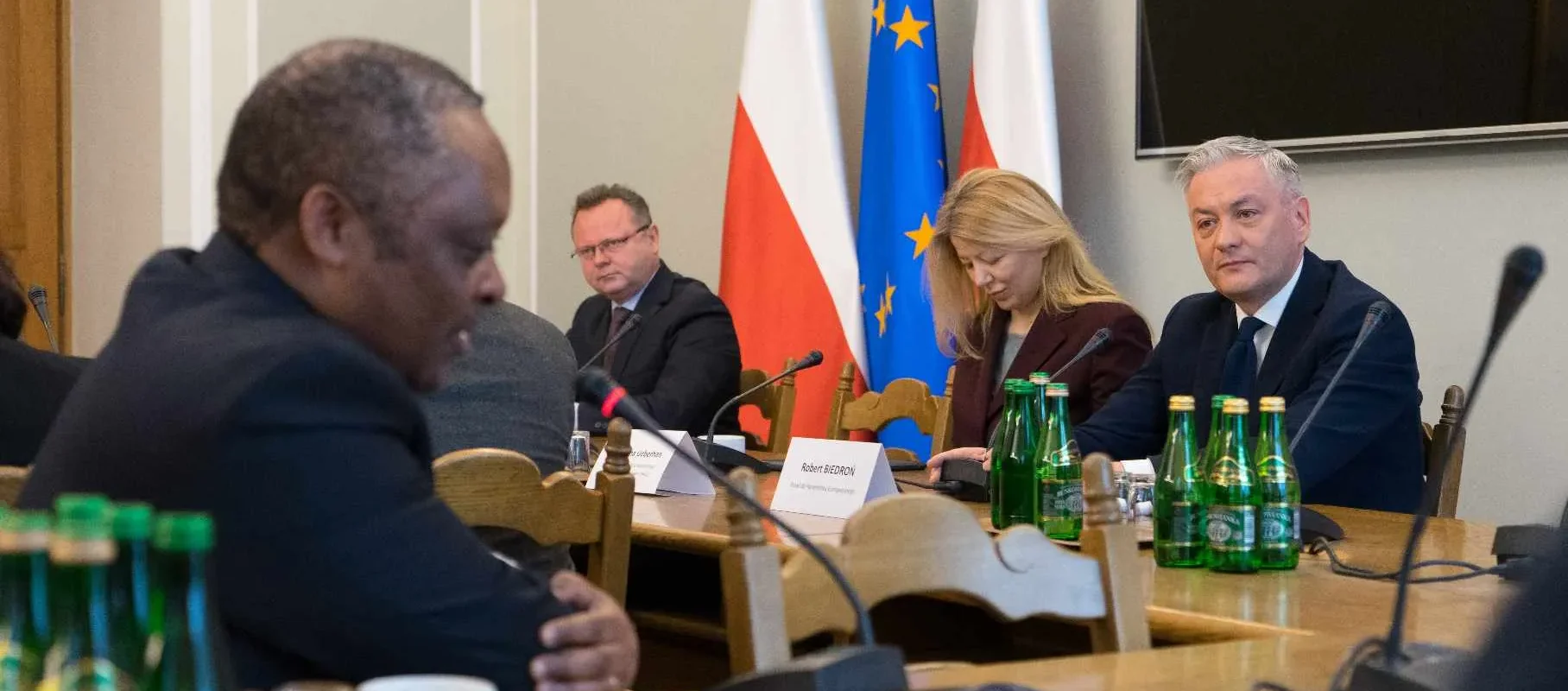 Uczestnicy spotkania z korpusem dyplomatycznym siedzą przy stole konferencyjnym, za którym stoją flagi Polski i Unii Europejskiej.