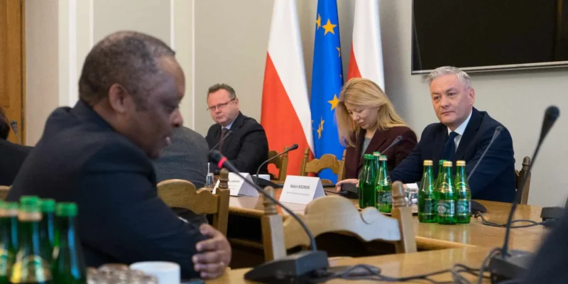 Uczestnicy spotkania z korpusem dyplomatycznym siedzą przy stole konferencyjnym, za którym stoją flagi Polski i Unii Europejskiej.