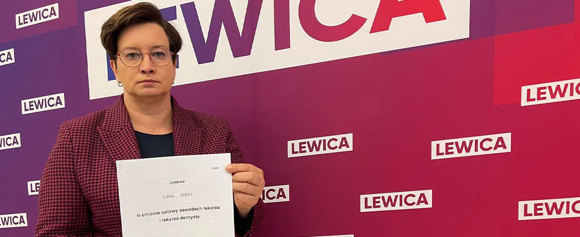 Kobieta w okularach trzyma dokument na tle banerów Lewicy, odnoszących się do projektu uchwały znoszącej klauzulę sumienia.