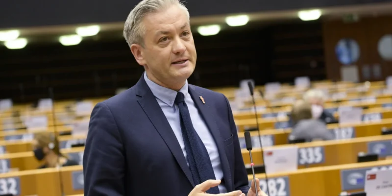 Mężczyzna w granatowym garniturze przemawia do mikrofonu w sali plenarnej podczas posiedzenia.