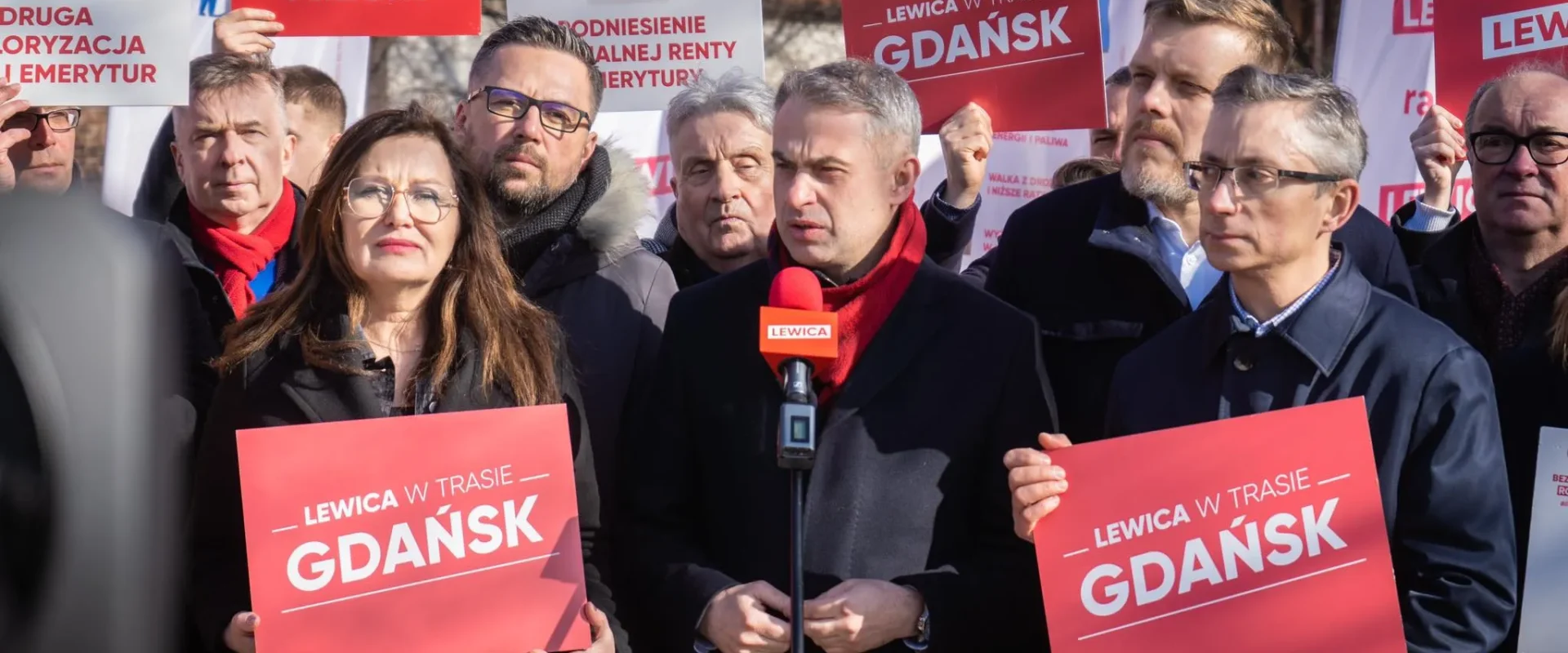 Na zdjęciu widoczna jest grupa osób na wiecu politycznym, trzymających plakaty z hasłem "Lewica w trasie Gdańsk".