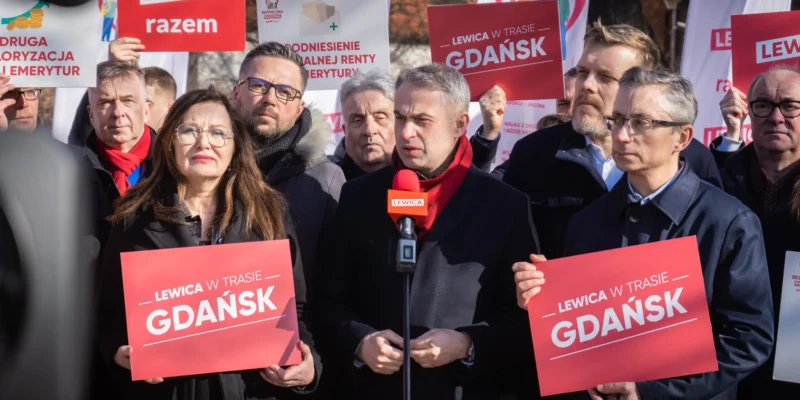 Na zdjęciu widoczna jest grupa osób na wiecu politycznym, trzymających plakaty z hasłem "Lewica w trasie Gdańsk".