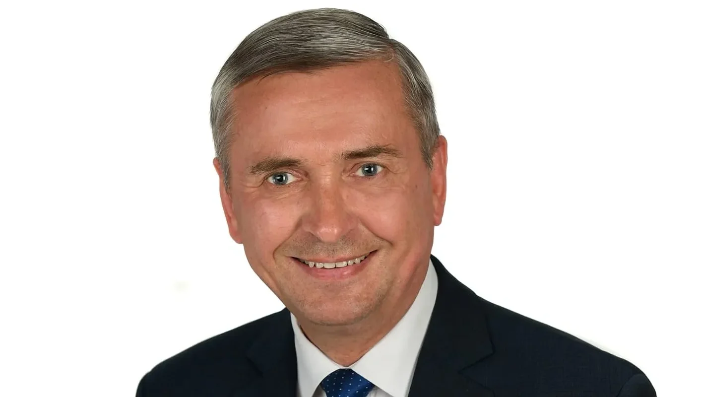 Portret uśmiechniętego mężczyzny w garniturze i granatowym krawacie na białym tle.