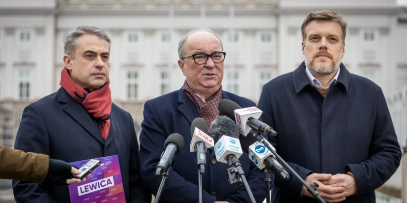 Na zdjęciu trzech mężczyzn stoi przed budynkiem, przedstawiając się jako przedstawiciele Lewicy, z mikrofonami i plakatem w dłoni.