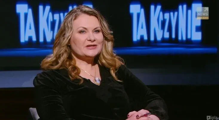 Kobieta o jasnych, falowanych włosach i czarnym ubraniu siedzi w studiu telewizyjnym i mówi, na tle widoczny jest podświetlony niebieski napis "TAK czy NIE".