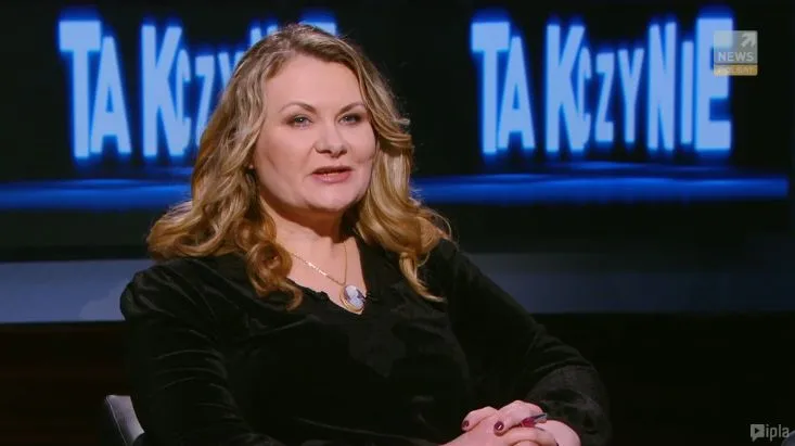 Kobieta o jasnych, falowanych włosach i czarnym ubraniu siedzi w studiu telewizyjnym i mówi, na tle widoczny jest podświetlony niebieski napis "TAK czy NIE".