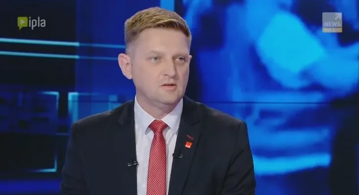 Mężczyzna w garniturze i czerwonym krawacie udziela wywiadu w studiu telewizyjnym na temat działań policji w Radomiu.