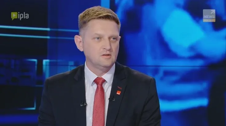 Mężczyzna w garniturze i czerwonym krawacie udziela wywiadu w studiu telewizyjnym na temat działań policji w Radomiu.