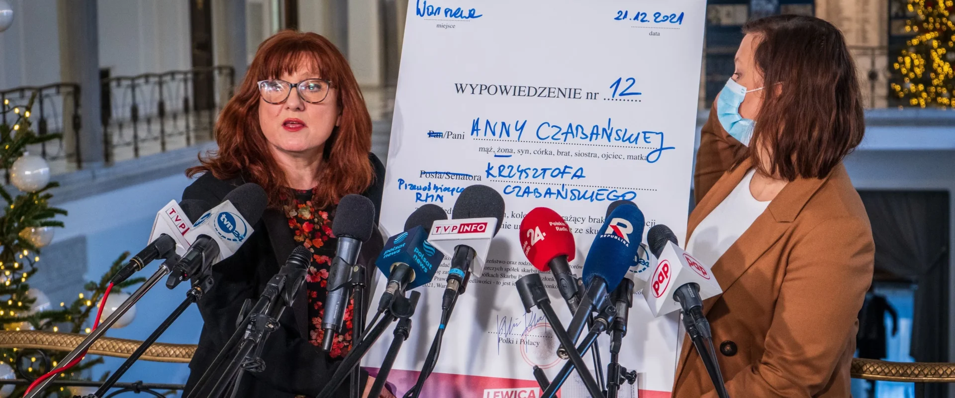 Na zdjęciu dwie kobiety prezentują dokument podczas konferencji prasowej, otoczone mikrofonami, w tle widoczna choinka.