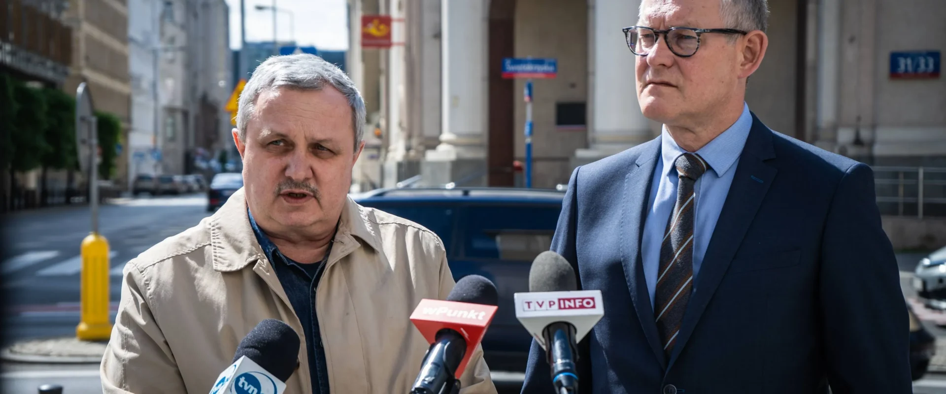 Dwóch mężczyzn na konferencji prasowej na ulicy, mówiących do mikrofonów, w kontekście Poczty Polskiej i postulatów obrony miejsc pracy oraz podwyżek.