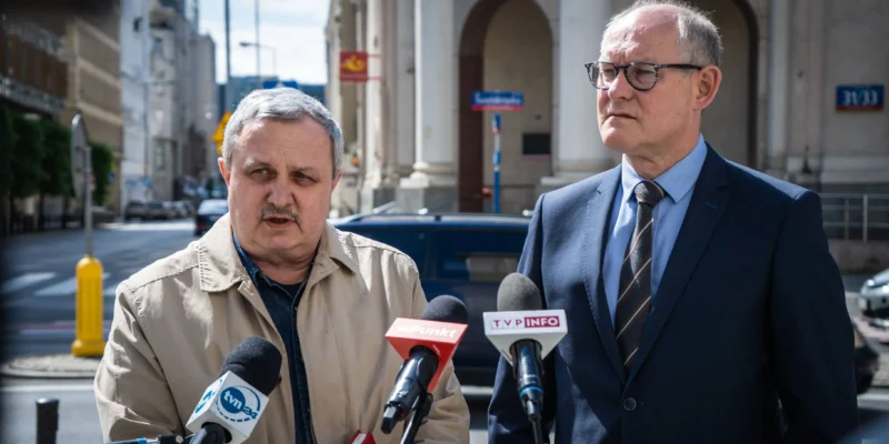 Dwóch mężczyzn na konferencji prasowej na ulicy, mówiących do mikrofonów, w kontekście Poczty Polskiej i postulatów obrony miejsc pracy oraz podwyżek.