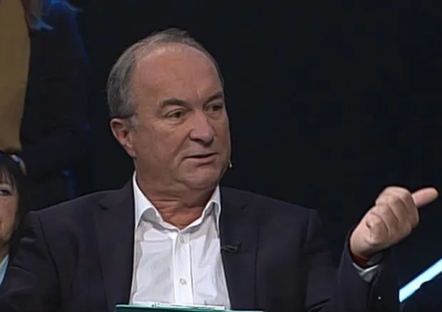 Mężczyzna w marynarce i białej koszuli gestykuluje podczas dyskusji w studiu telewizyjnym o służbach mundurowych.