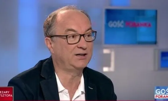 Mężczyzna w okularach i marynarce mówi podczas rozmowy w telewizyjnym studio.