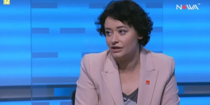 Kobieta w jasnoróżowej marynarce siedzi i rozmawia w studiu telewizyjnym na niebieskim tle z widocznym logotypem stacji.