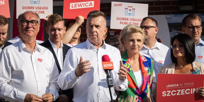 Grupa polityków Lewicy podczas konferencji prasowej, z mężczyzną w białej koszuli mówiącym do mikrofonu, na tle plakatów z logiem Lewicy i hasłem „Dobre usługi publiczne”.