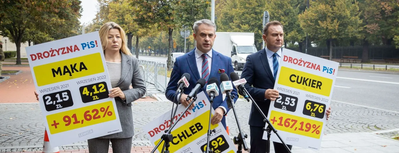 Na zdjęciu przedstawieni są trzej politycy podczas konferencji prasowej, trzymający plakaty z informacjami o wzroście cen żywności, takich jak chleb, mąka i cukier.