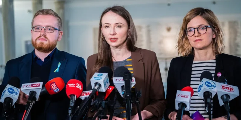 Trzy osoby stoją na konferencji prasowej otoczone licznymi mikrofonami; pośrodku przemawia osoba, odnosząc się do inflacji i twierdząc, że dziś nie tracą milionerzy, lecz emeryci i osoby zarabiające średnią krajową.