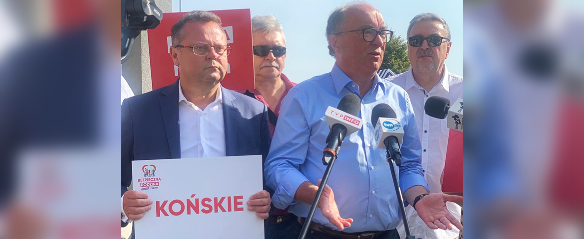 Na zdjęciu widoczni są mężczyźni podczas konferencji prasowej, z jednym z nich trzymającym transparent z napisem