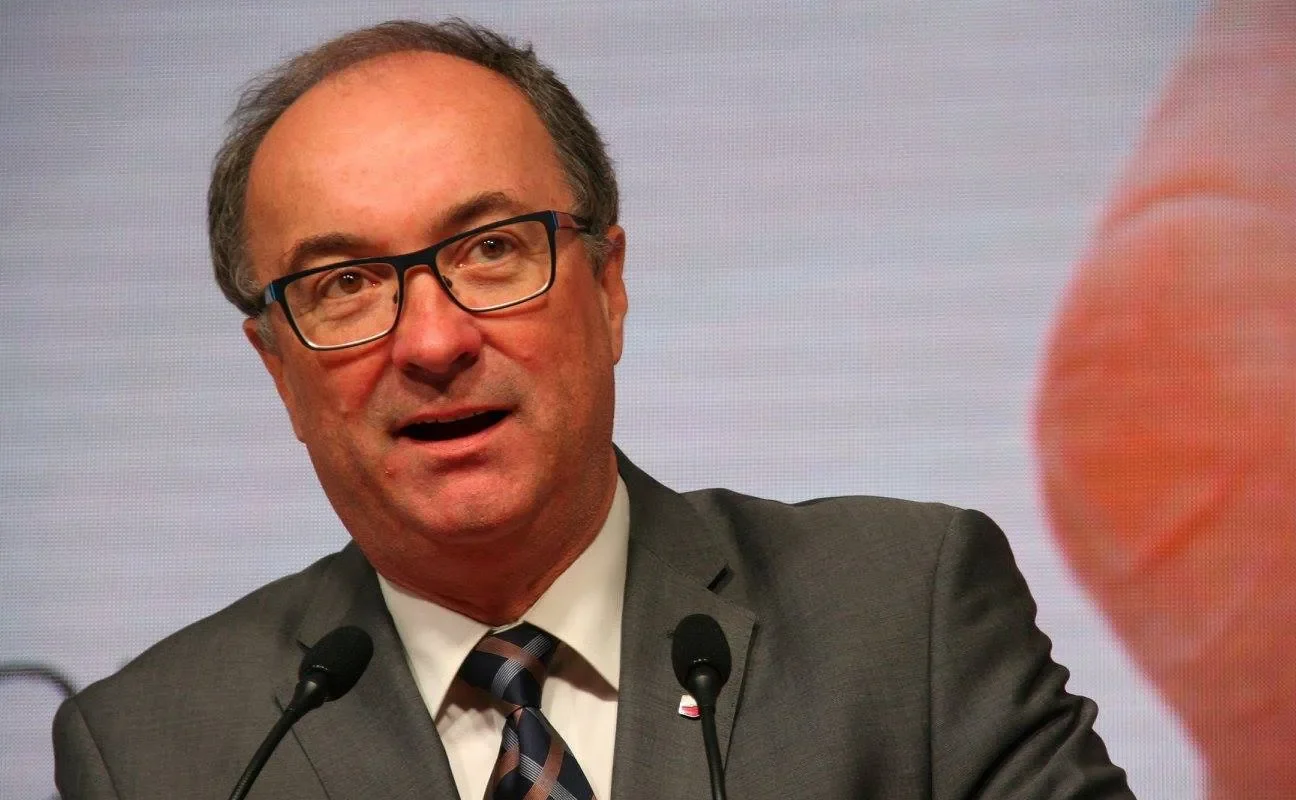 Polityk w garniturze i okularach przemawia przy dwóch mikrofonach na tle ekranu podczas wystąpienia o stosunkach z Izraelem.