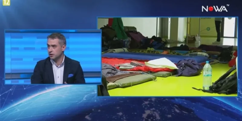 Split-screen: po lewej mężczyzna w marynarce rozmawia w studiu telewizyjnym, po prawej rozłożone śpiwory, plecaki i butelka wody na podłodze sali.