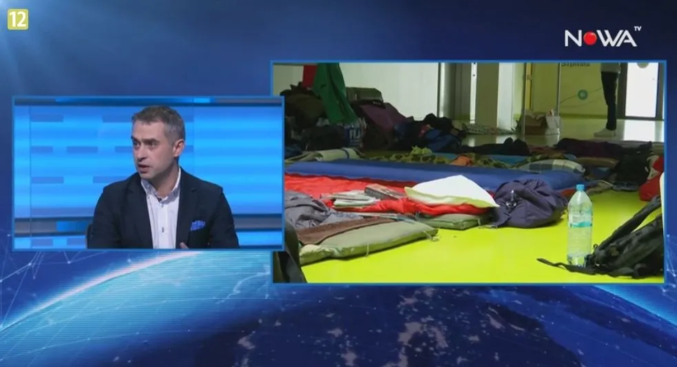 Split-screen: po lewej mężczyzna w marynarce rozmawia w studiu telewizyjnym, po prawej rozłożone śpiwory, plecaki i butelka wody na podłodze sali.