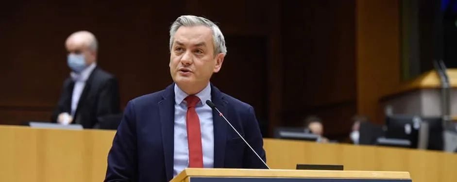 Na zdjęciu mężczyzna w garniturze przemawia do zgromadzenia w sali obiadowej.