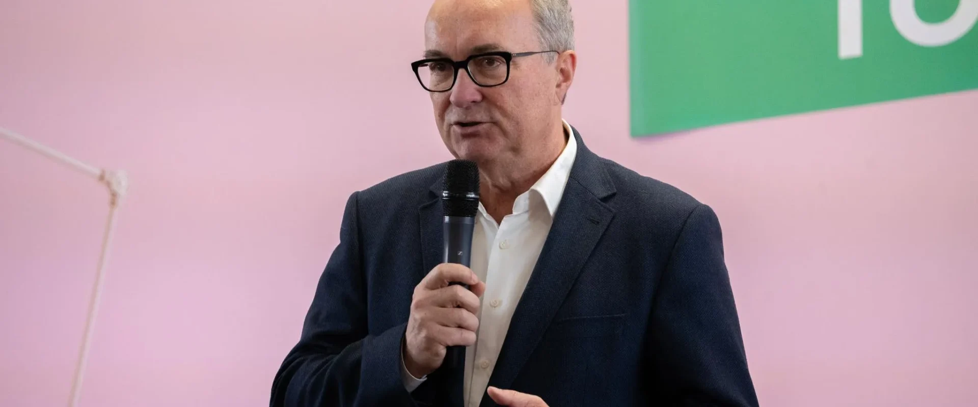 Niezidentyfikowany mężczyzna w granatowym garniturze przemawia do mikrofonu podczas wydarzenia dot. aborcji, stojąc na tle różowej ściany.