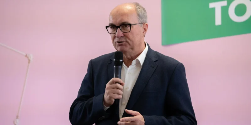 Niezidentyfikowany mężczyzna w granatowym garniturze przemawia do mikrofonu podczas wydarzenia dot. aborcji, stojąc na tle różowej ściany.