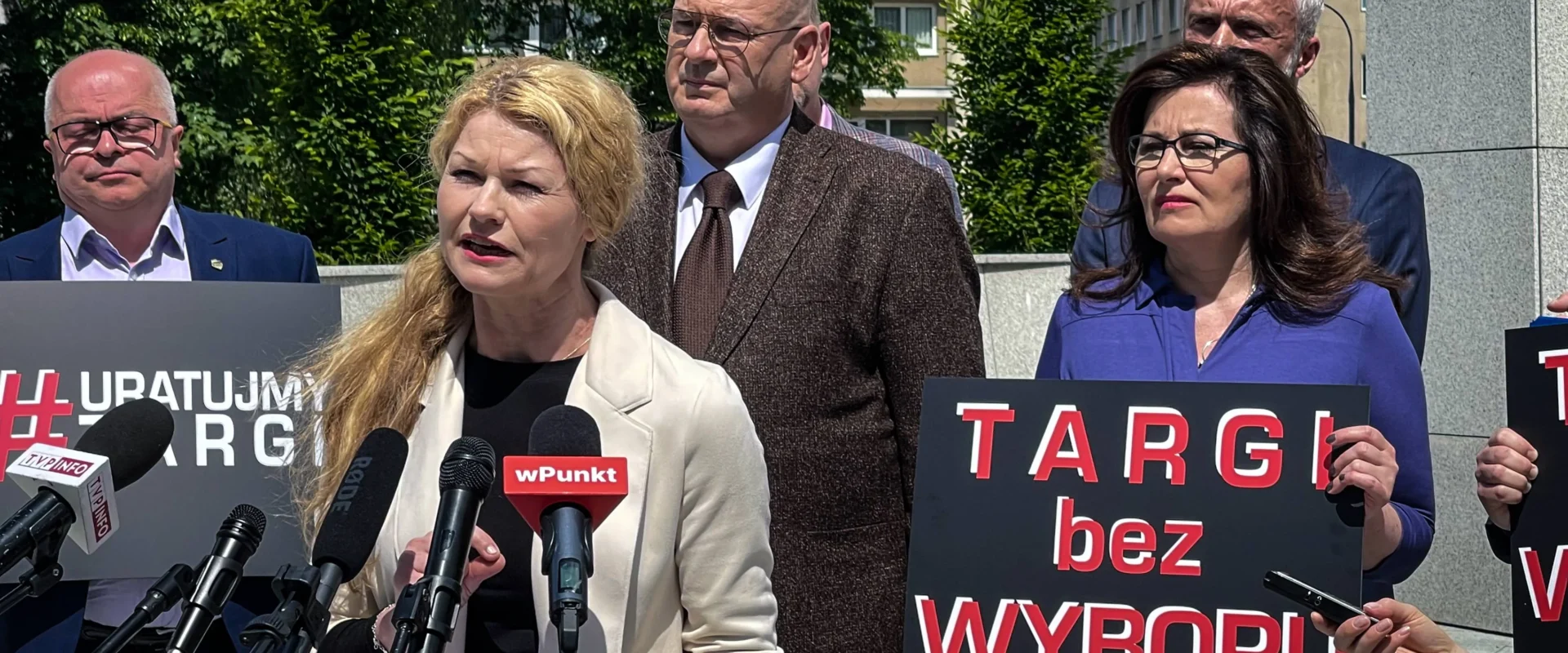 Grupa osób podczas konferencji prasowej trzyma plakaty z napisem „TARGI bez WYBORU” i apeluje do rządu o konkretne daty otwarcia branży targowej oraz wsparcie finansowe.