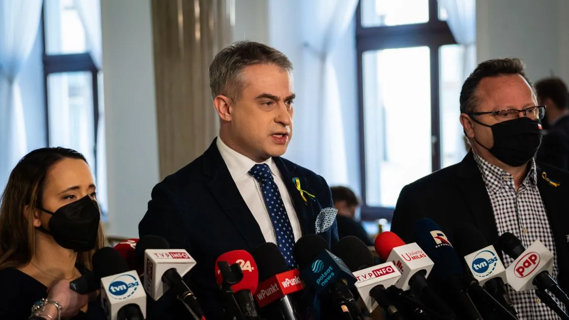 Na zdjęciu trzech mężczyzn i jedna kobieta stoją przed mikrofonami podczas konferencji prasowej.