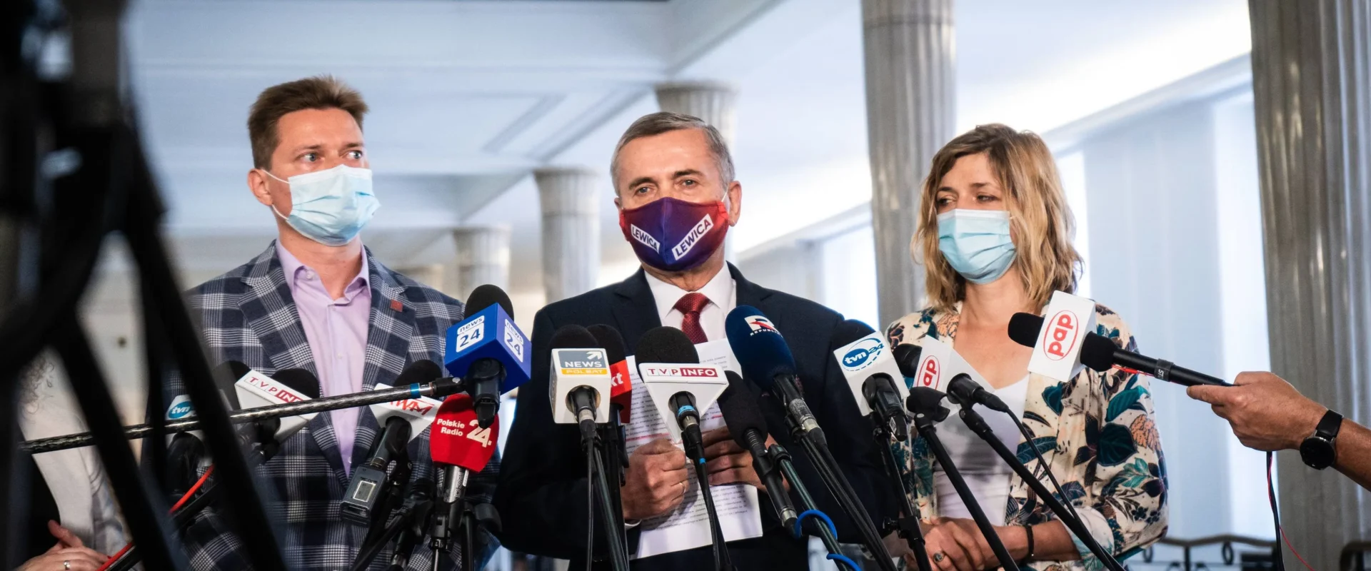 Grupa osób w maseczkach na konferencji prasowej stojąca za licznymi mikrofonami, omawia emerytury stażowe po 35 latach pracy kobiet i 40 latach pracy mężczyzn.