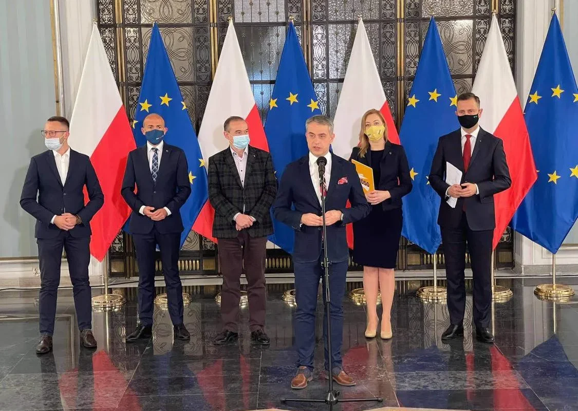 Grupa polityków w maseczkach stoi podczas konferencji prasowej na tle flag Polski i Unii Europejskiej, prezentując wspólny wniosek opozycji o powołanie sejmowej komisji śledczej w obronie niezależności NIK.