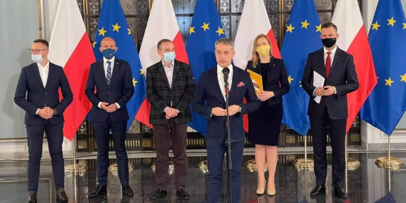 Grupa polityków w maseczkach stoi podczas konferencji prasowej na tle flag Polski i Unii Europejskiej, prezentując wspólny wniosek opozycji o powołanie sejmowej komisji śledczej w obronie niezależności NIK.