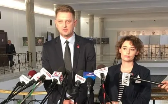 Mężczyzna i kobieta stoją przed szeregiem mikrofonów podczas konferencji prasowej, wypowiadając się o niedoskonałym realizowaniu testamentu Kality.