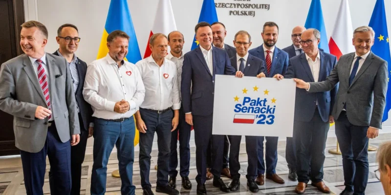 Grupa mężczyzn w garniturach prezentuje plakat z napisem „Pakt Senacki 23” na tle flag Polski i Unii Europejskiej.
