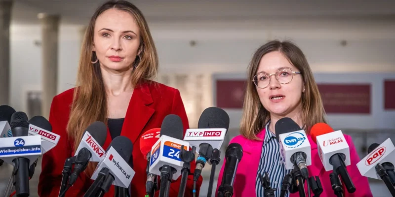 Na zdjęciu dwie kobiety stoją przy mównicy otoczonej mikrofonami, uczestnicząc w konferencji prasowej.