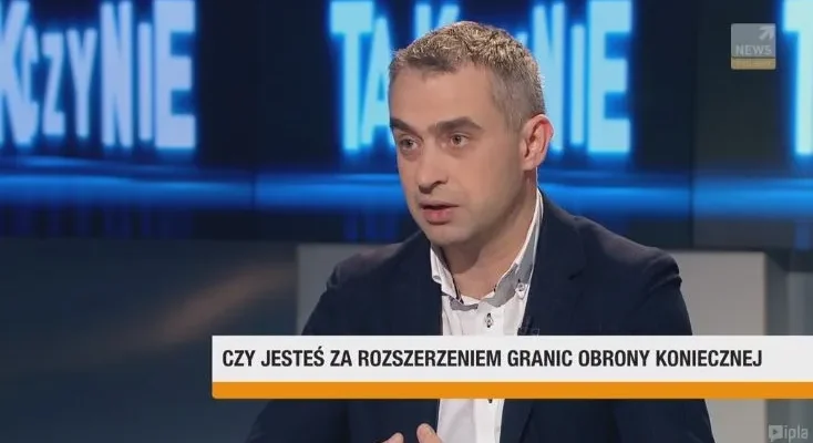 Mężczyzna w marynarce wypowiada się w studiu telewizyjnym, a na dolnym pasku widoczny jest napis: "CZY JESTEŚ ZA ROZSZERZENIEM GRANIC OBRONY KONIECZNEJ".