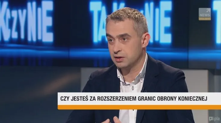 Mężczyzna w marynarce wypowiada się w studiu telewizyjnym, a na dolnym pasku widoczny jest napis: "CZY JESTEŚ ZA ROZSZERZENIEM GRANIC OBRONY KONIECZNEJ".