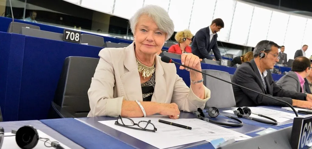 Kobieta siedzi przy mikrofonie w sali obrad Parlamentu Europejskiego, z dokumentami i słuchawkami przed sobą, podczas dyskusji o programie Erasmus+.