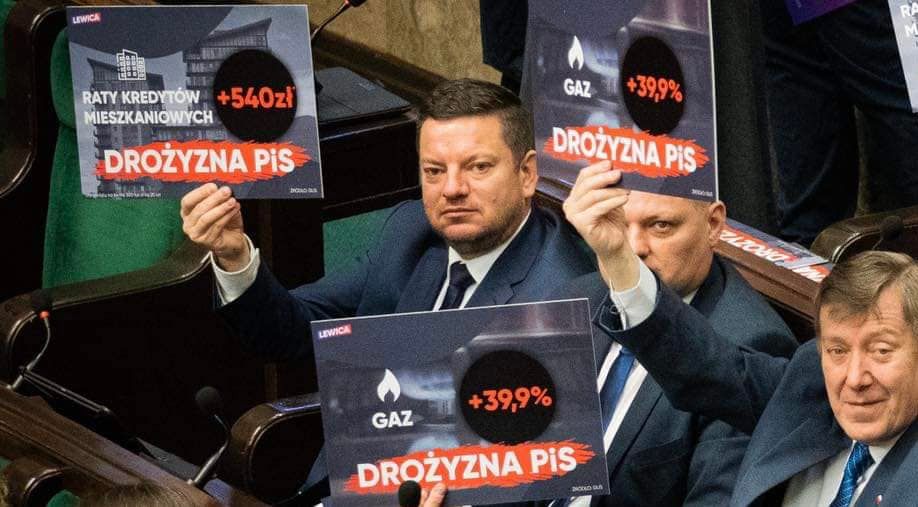 Na zdjęciu widoczni są mężczyźni w garniturach trzymający plakaty z hasłami o wzrostach kosztów kredytów i gazu, protestując w sejmie.