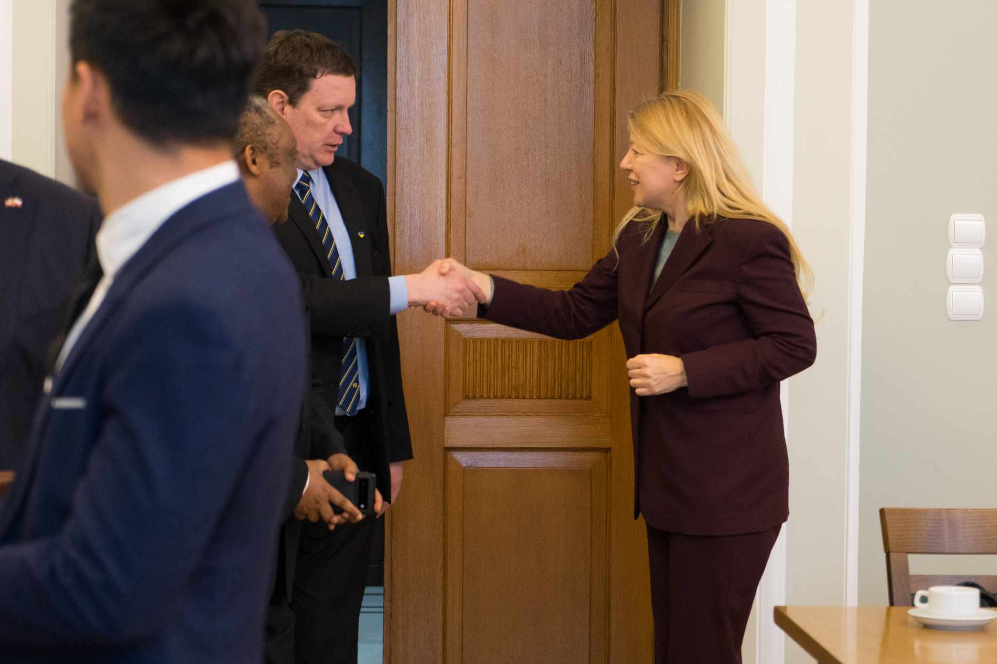 Osoby w garniturach witają się, ściskając dłonie przy wejściu podczas spotkania z korpusem dyplomatycznym.