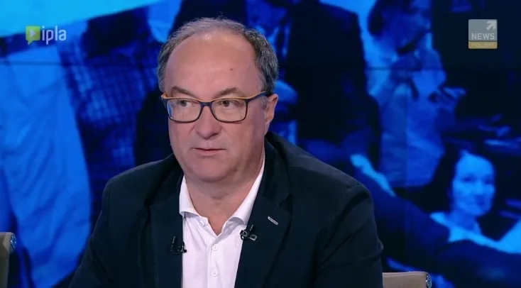 Polityk w okularach i marynarce siedzi w studiu telewizyjnym podczas wywiadu (temat: prezydent i sprawa Kamińskiego).