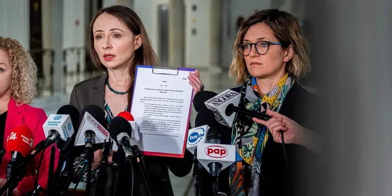 Trzy kobiety podczas konferencji prasowej stoją za mikrofonami; jedna z nich trzyma dokument z projektem ustawy o drugiej waloryzacji rent i emerytur.