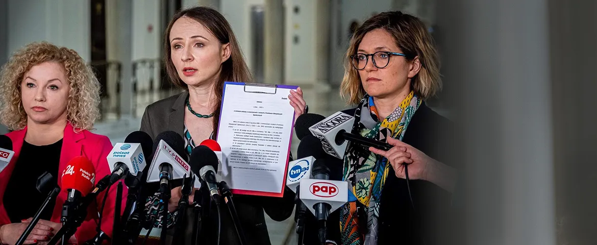 Trzy kobiety podczas konferencji prasowej stoją za mikrofonami; jedna z nich trzyma dokument z projektem ustawy o drugiej waloryzacji rent i emerytur.